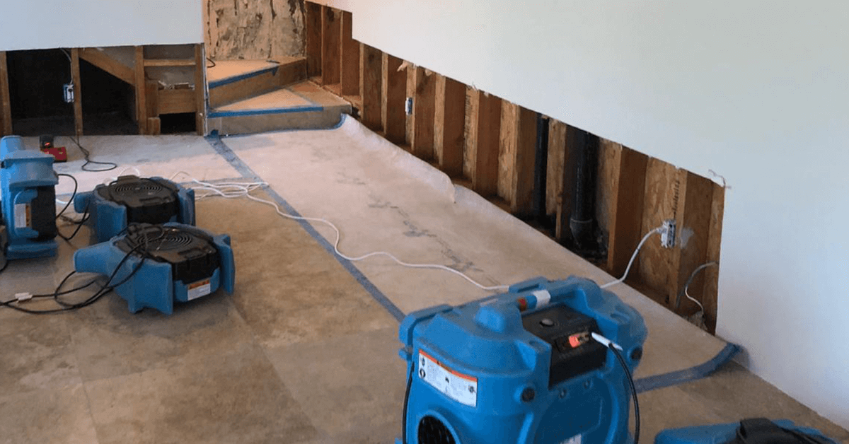 Dehumidifiers drying a room damaged by water. Exposed framing, partial wall, and concrete floor.