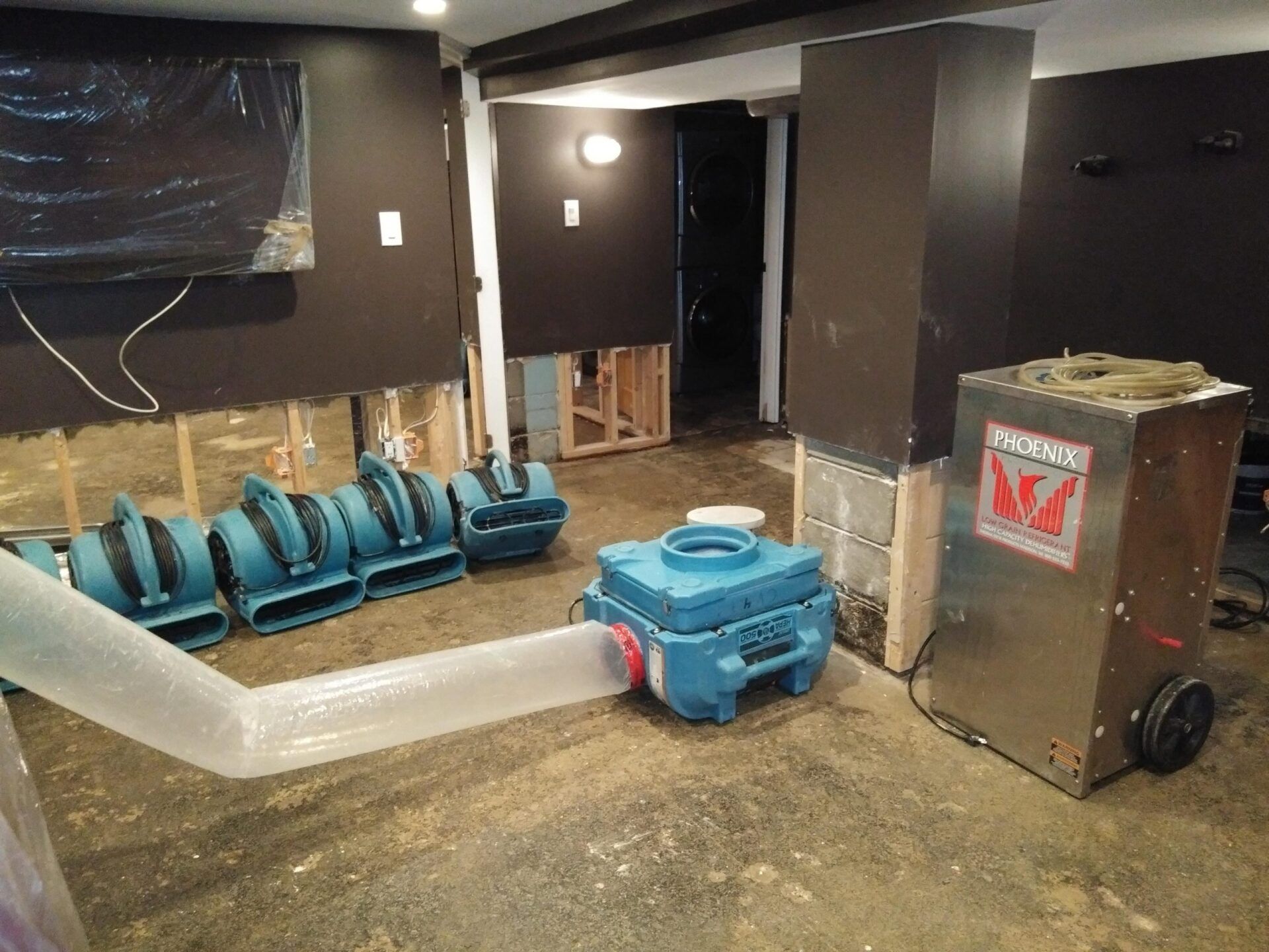Basement with water damage, drying equipment deployed; dark walls, exposed studs, debris.