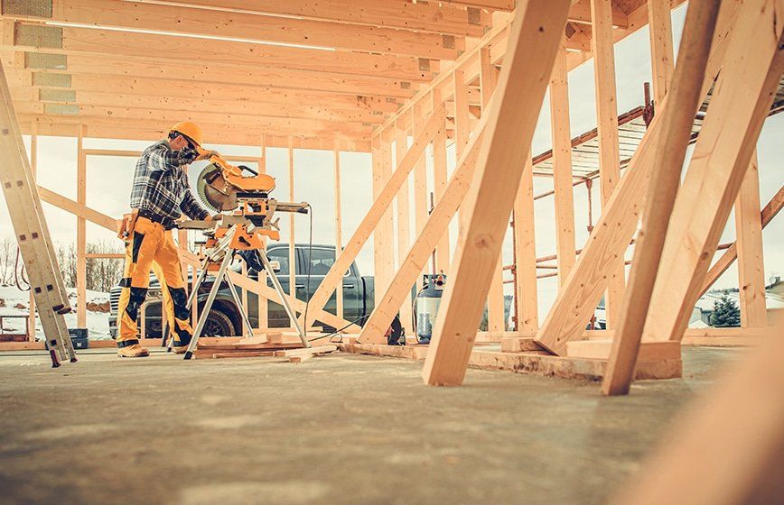 Construction worker uses a saw to cut wood beams inside a building under construction.