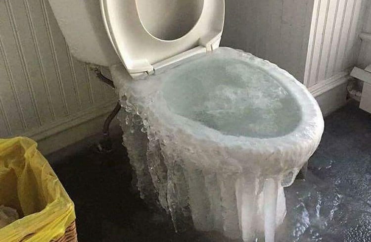 Toilet covered in ice, likely frozen due to cold weather. Water frozen over the bowl and running down the sides.