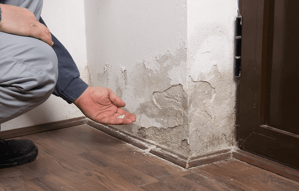 Person inspecting peeling paint on a wall near a doorway, indicating moisture damage.