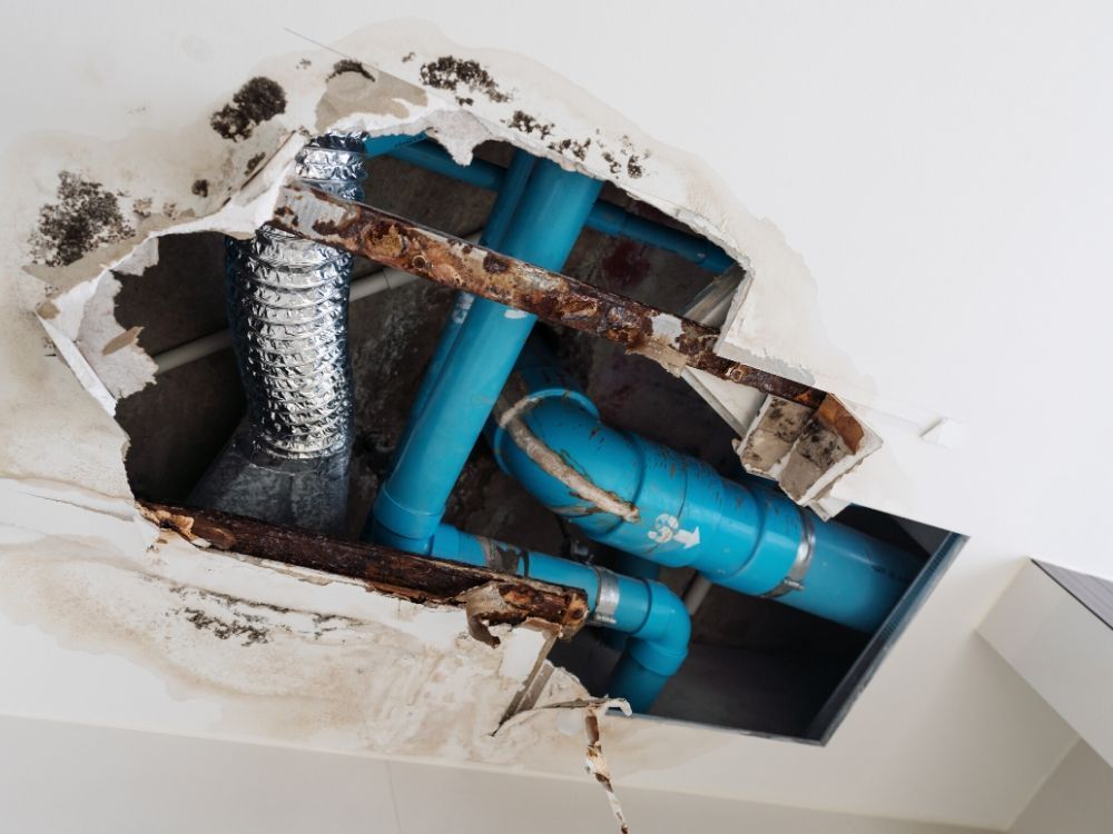Damaged ceiling exposing blue pipes, ductwork, and rusted metal framing. Water damage visible.