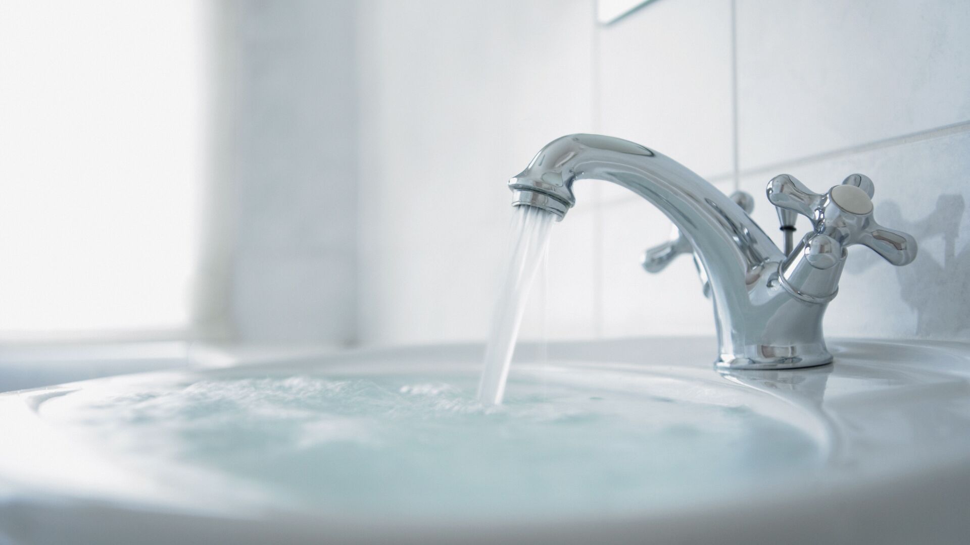 Water flowing from a chrome faucet into a white, filled sink.
