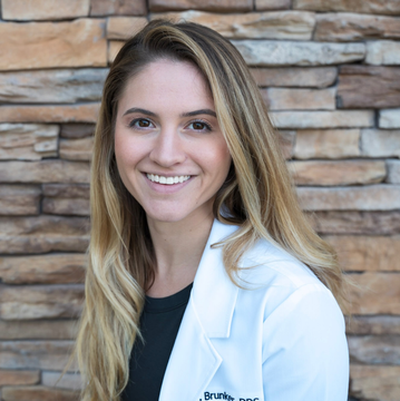 Best family dentist in Lee's Summit, MO and surrounding areas. A woman in a lab coat is smiling in front of a brick wall