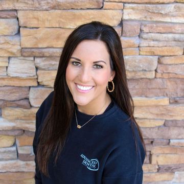 A woman is smiling in front of a brick wall.