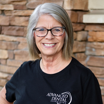 Best cosmetic dentist in Lee's Summit, MO and surrounding areas. A woman wearing glasses is smiling in front of a brick wall.