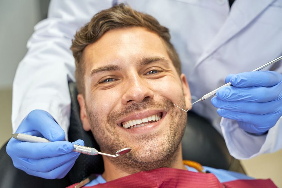 A man is smiling while having his teeth examined by a dentist | Dental crowns and bridges in Lees Summit MO