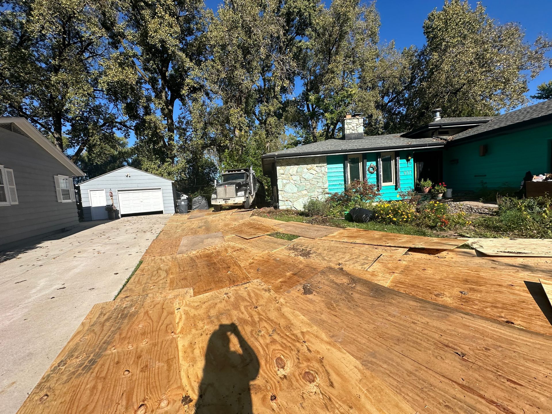 A shadow of a person is cast on a pile of dirt in front of a house.