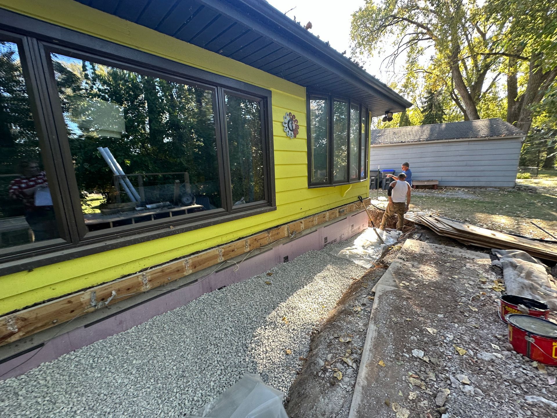 A yellow house with a lot of windows is being remodeled.