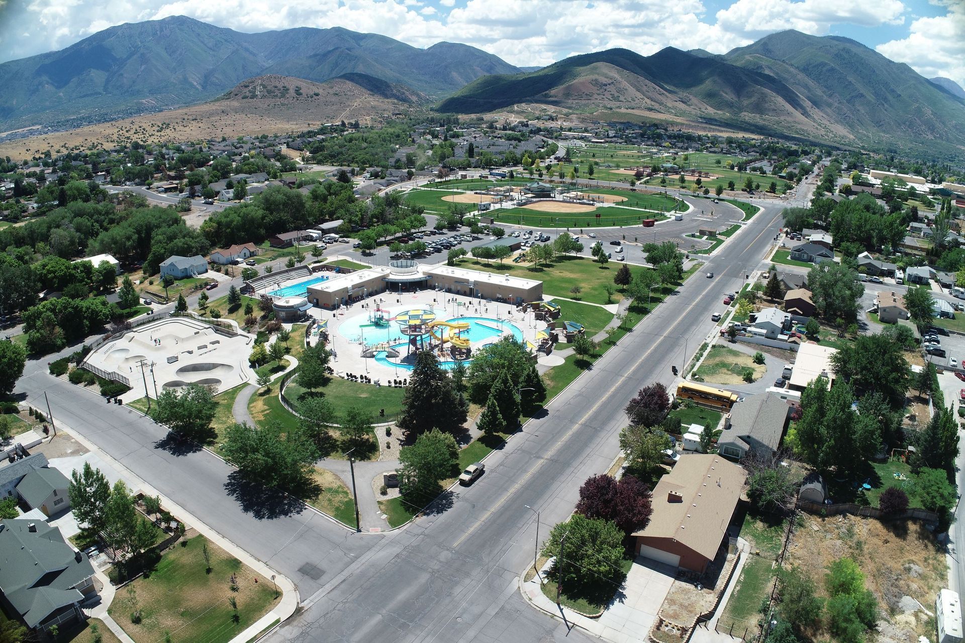 Aerial view of a suburban neighborhood with a swimming pool, roads, trees, and mountains in the background