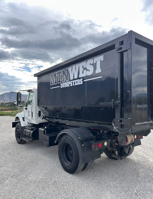 Black dump truck parked on gravel, side view with white phone number and logo on the bed