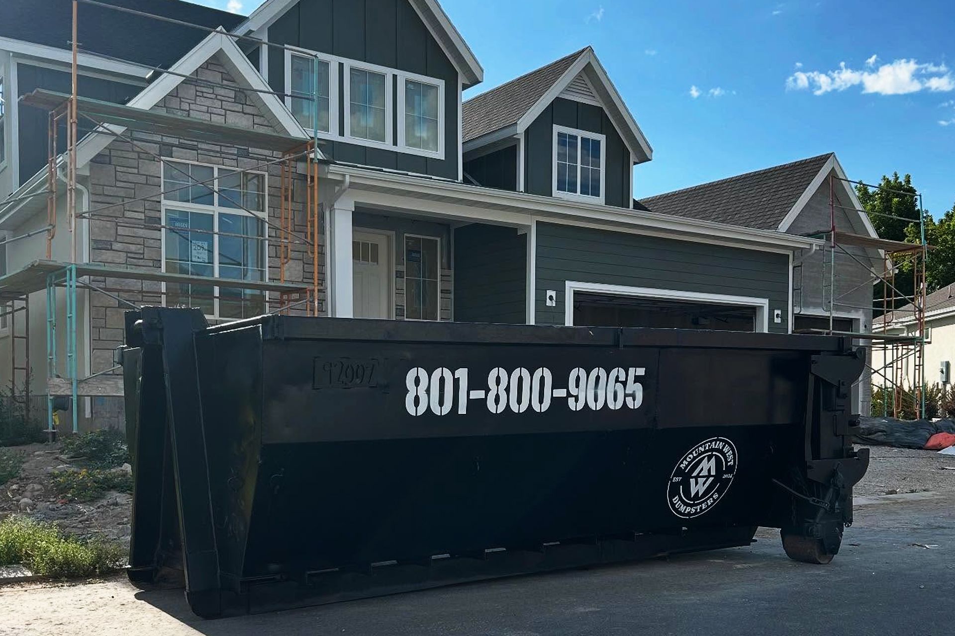 Black dumpster with 801-800-9865 in front of a suburban house under construction