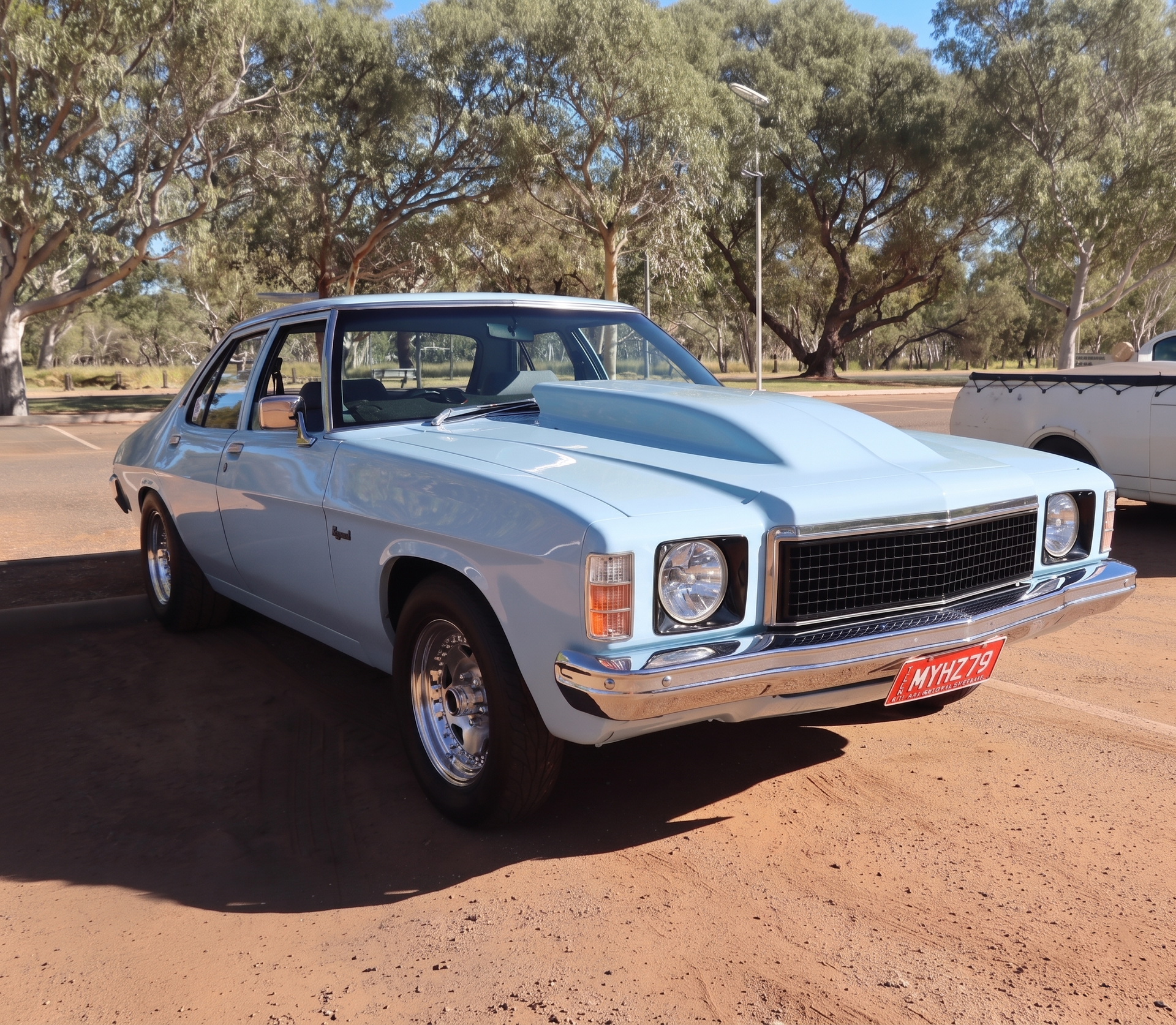 Classic white sedan parked on dirt road under trees, front view