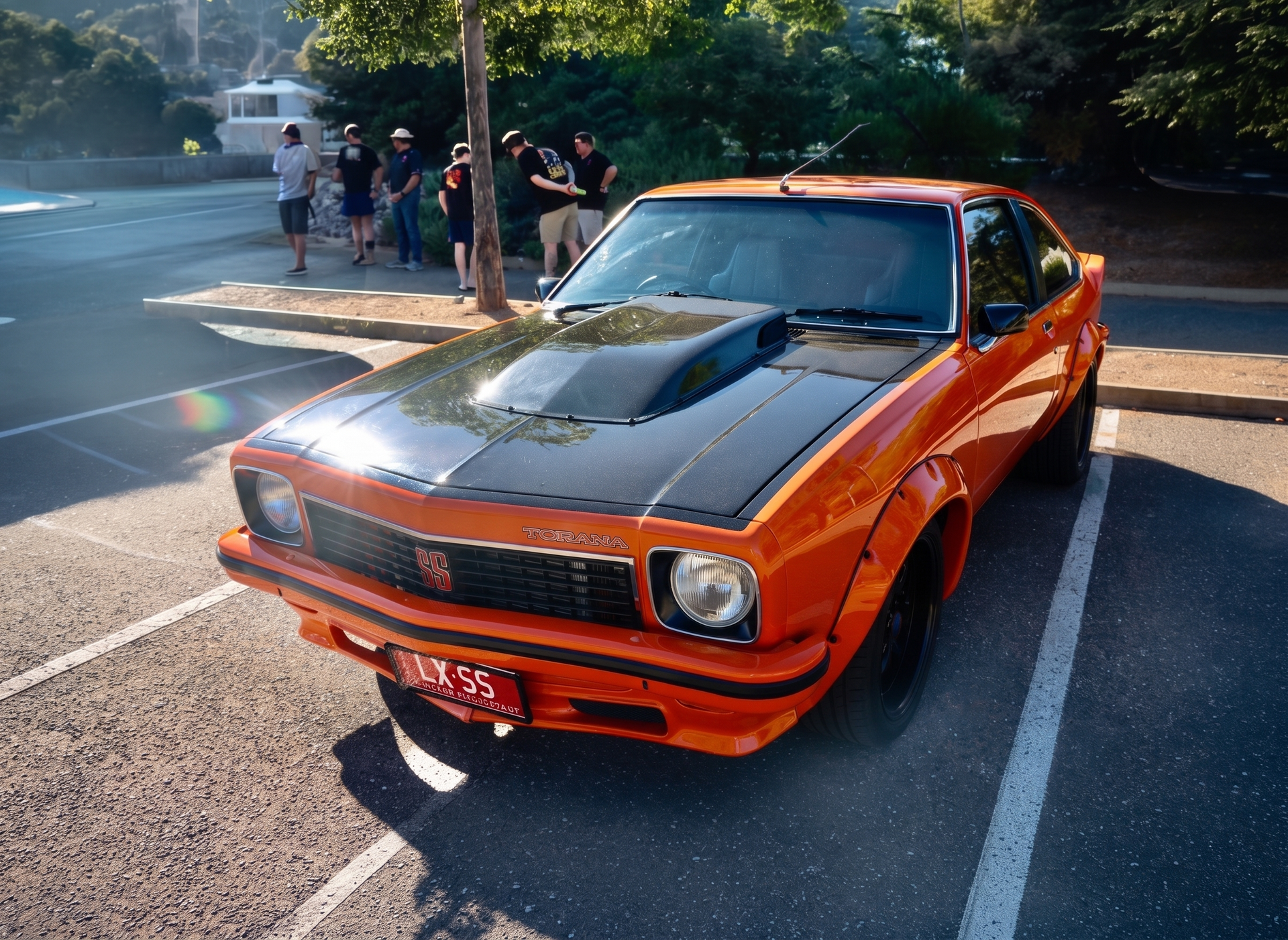 Orange classic muscle car parked on a road with people in the background