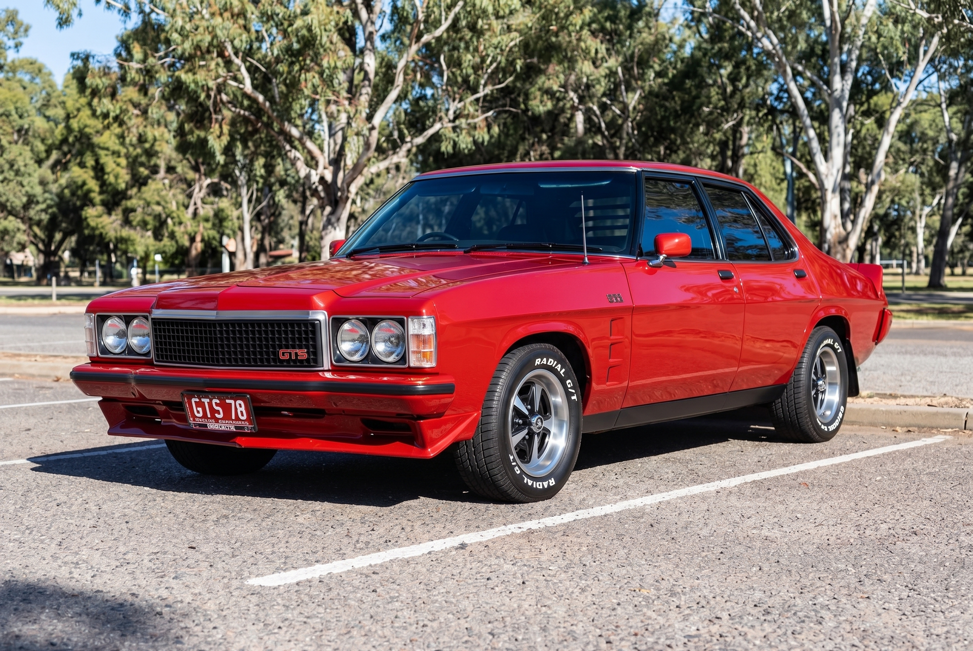 Red classic muscle car parked in a lot with trees in the background