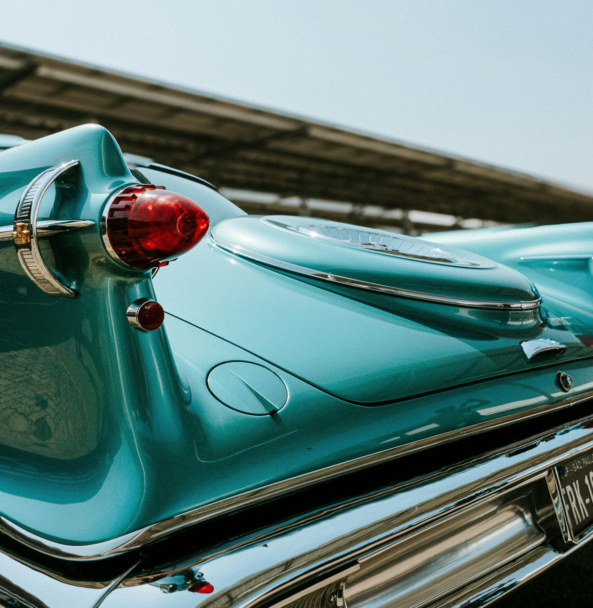 Close-up of a turquoise vintage car tail fin with a red taillight, parked outdoors