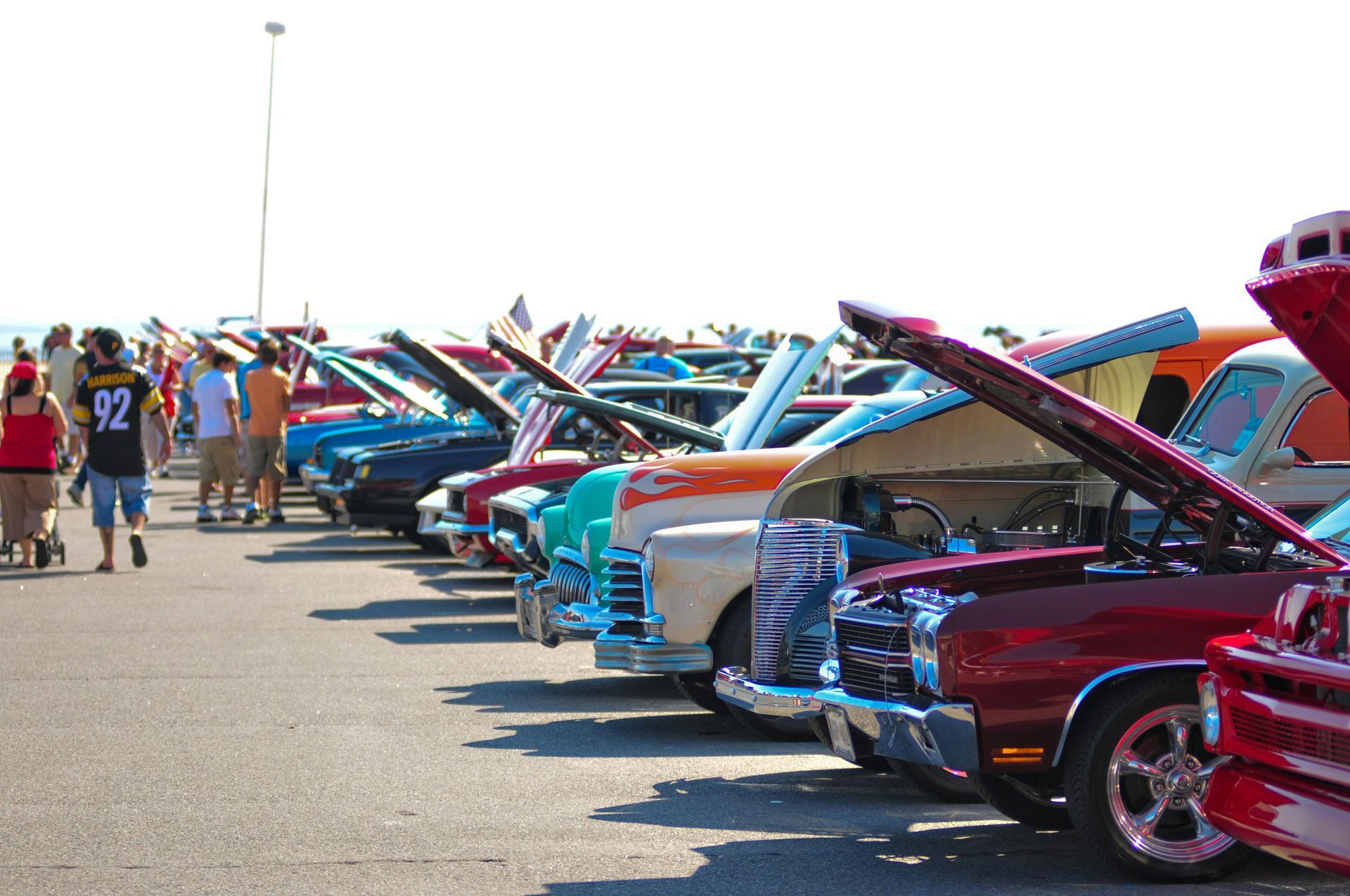 Classic cars lined up at a car show with hoods open, including red, blue, and turquoise vehicles.
