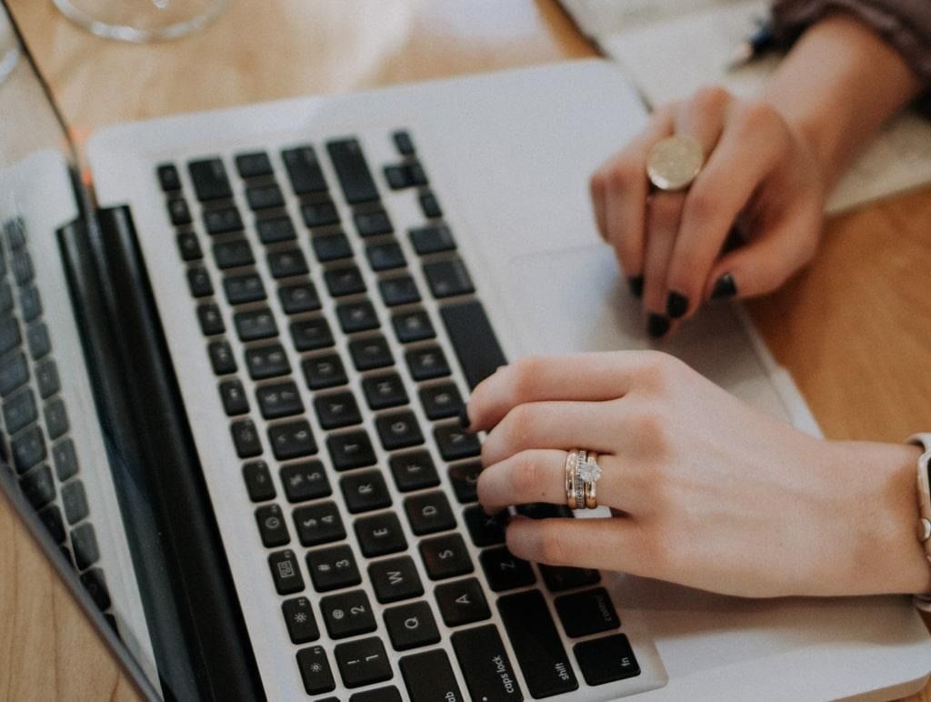 Hands typing on a laptop beside a notebook on a wooden desk