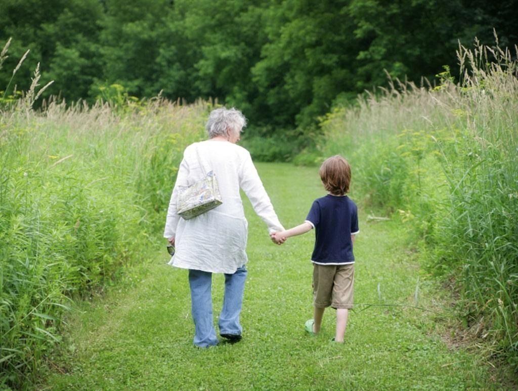 Two people holding hands walking along a grassy path through tall greenery