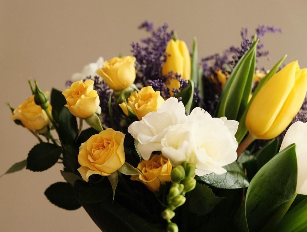 Yellow and white flowers in a bouquet with green leaves and purple accents