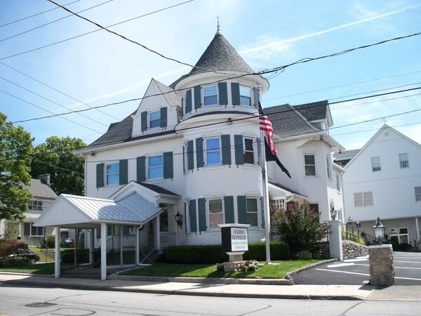 Victorian white house with blue shutters, turret, and American flag on a sunny street corner