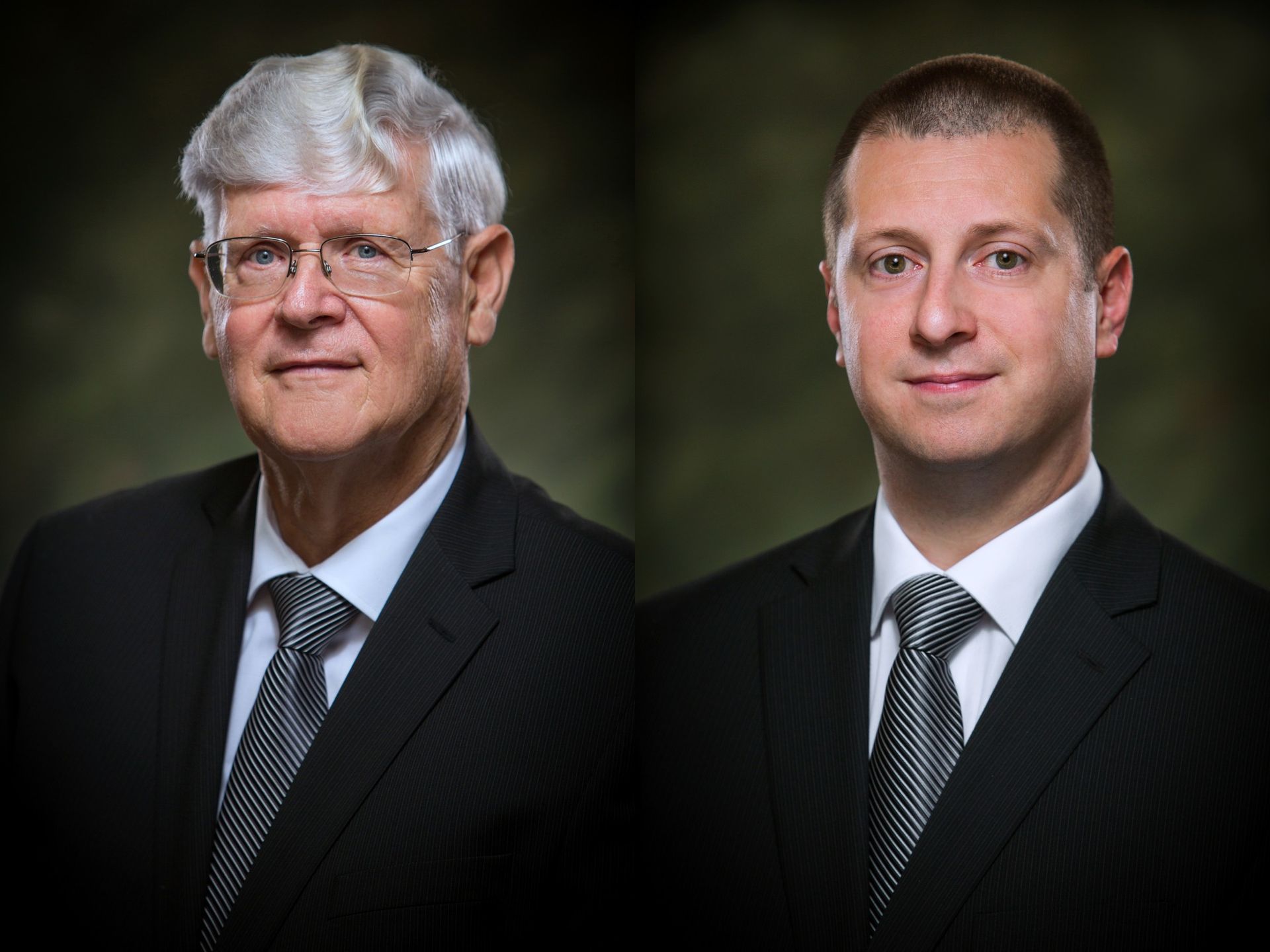 Two men in dark suits and ties pose against a blurred dark background.