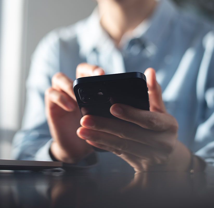 Person holding a smartphone at a table, using it indoors with a blurred background