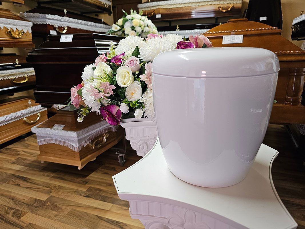 White urn-shaped funeral casket beside pink and white flowers in a chapel