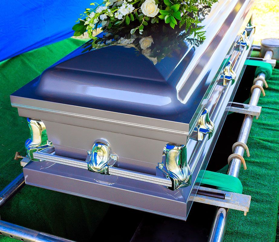 Silver coffin with white flowers and chrome handles on a green carpeted platform