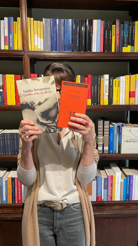 Una persona tiene in mano due libri davanti a una libreria colorata.