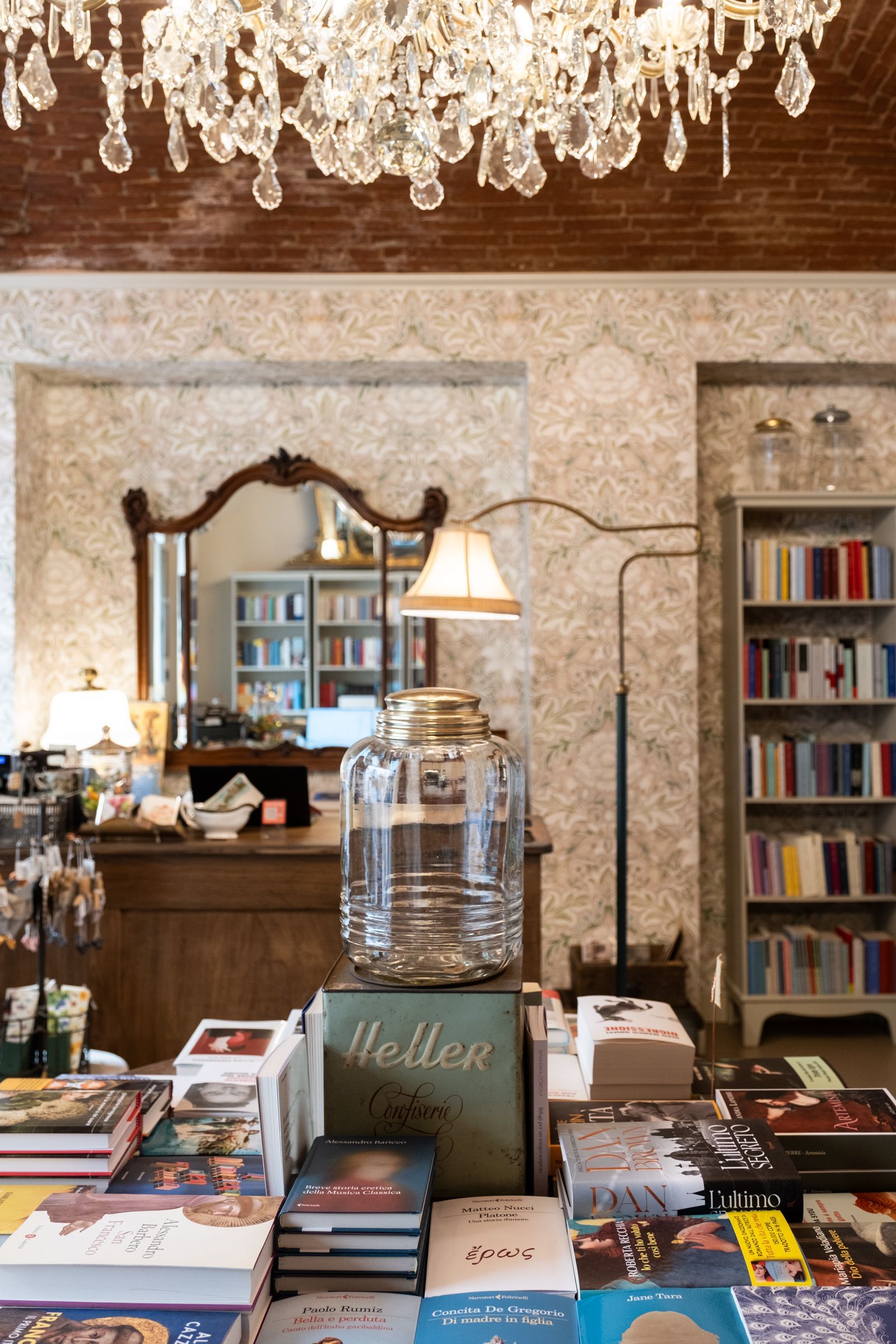 Tavolo espositivo di una libreria con libri, uno specchio e un lampadario sopra.