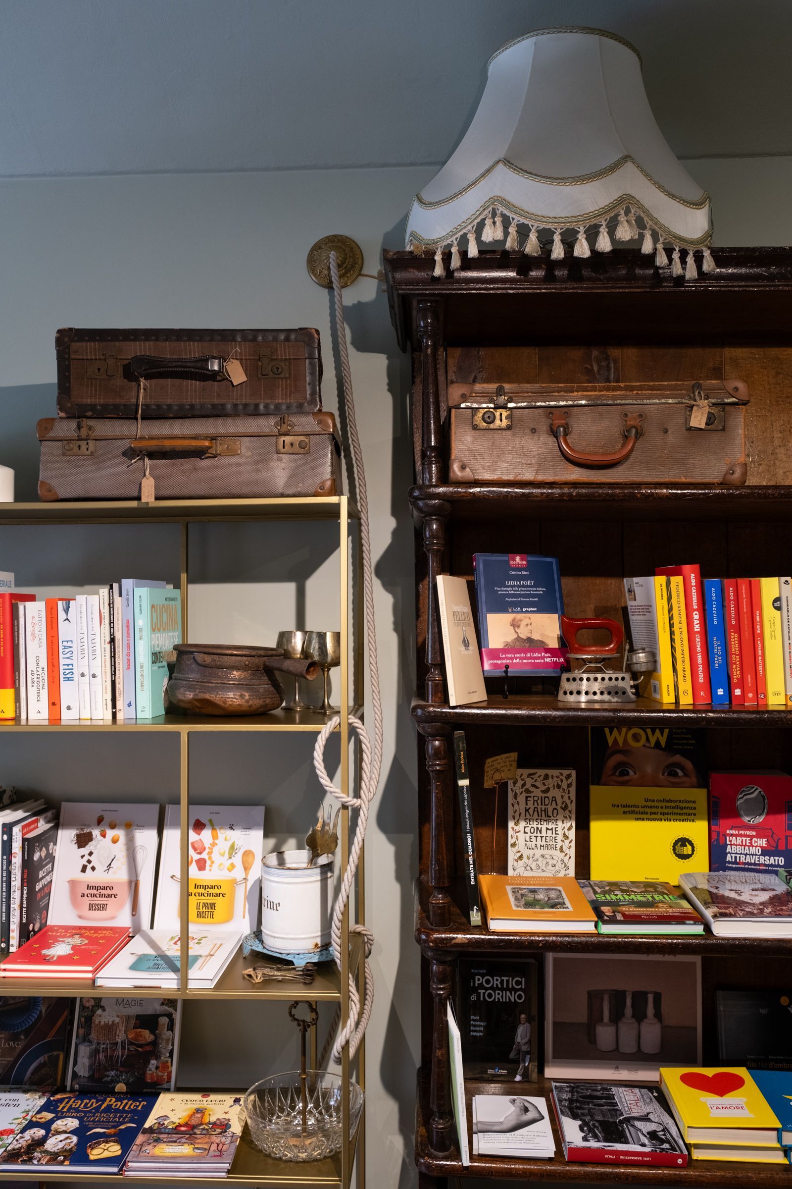 In una stanza accogliente, una libreria con libri colorati e soprammobili, sormontata da un paralume bianco.
