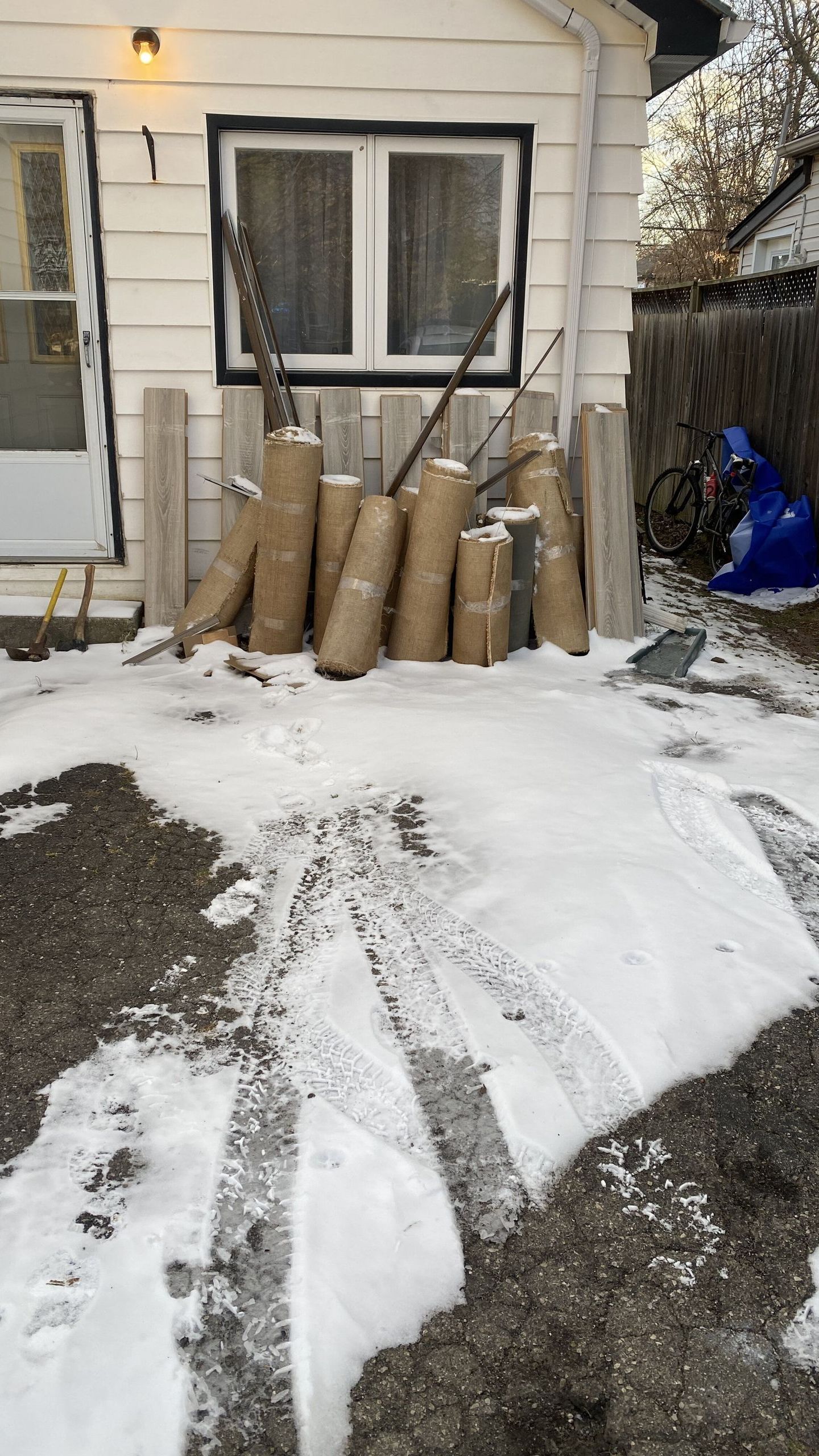 Snowy backyard with several rolled cardboard tubes leaning against a house under a window