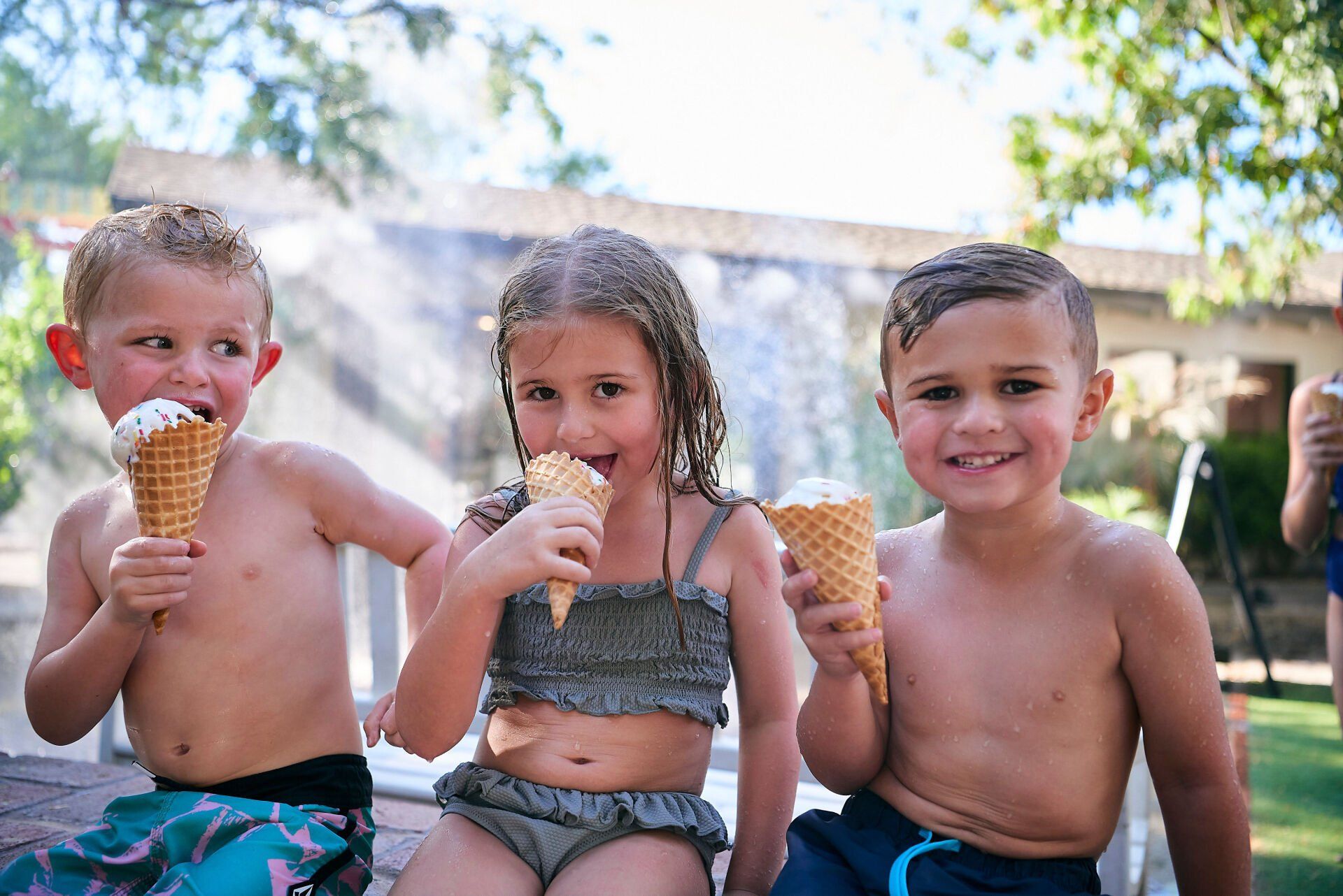 Three young children are eating ice cream cones outside of splurge ice cream & candy shop