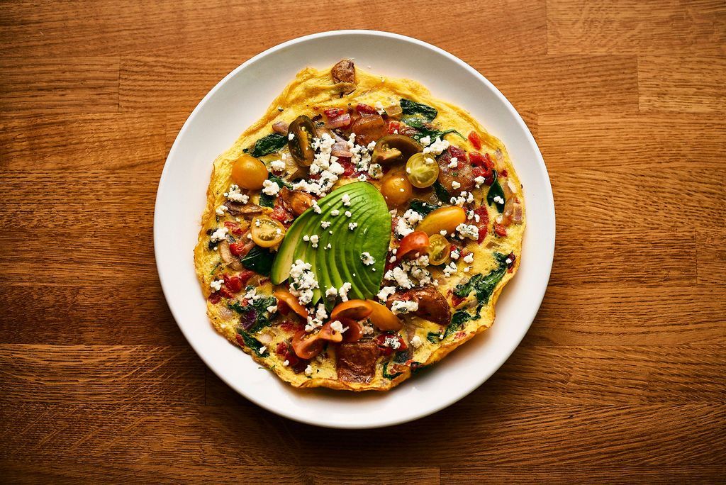 A white plate topped with an omelet and avocado on a wooden table.