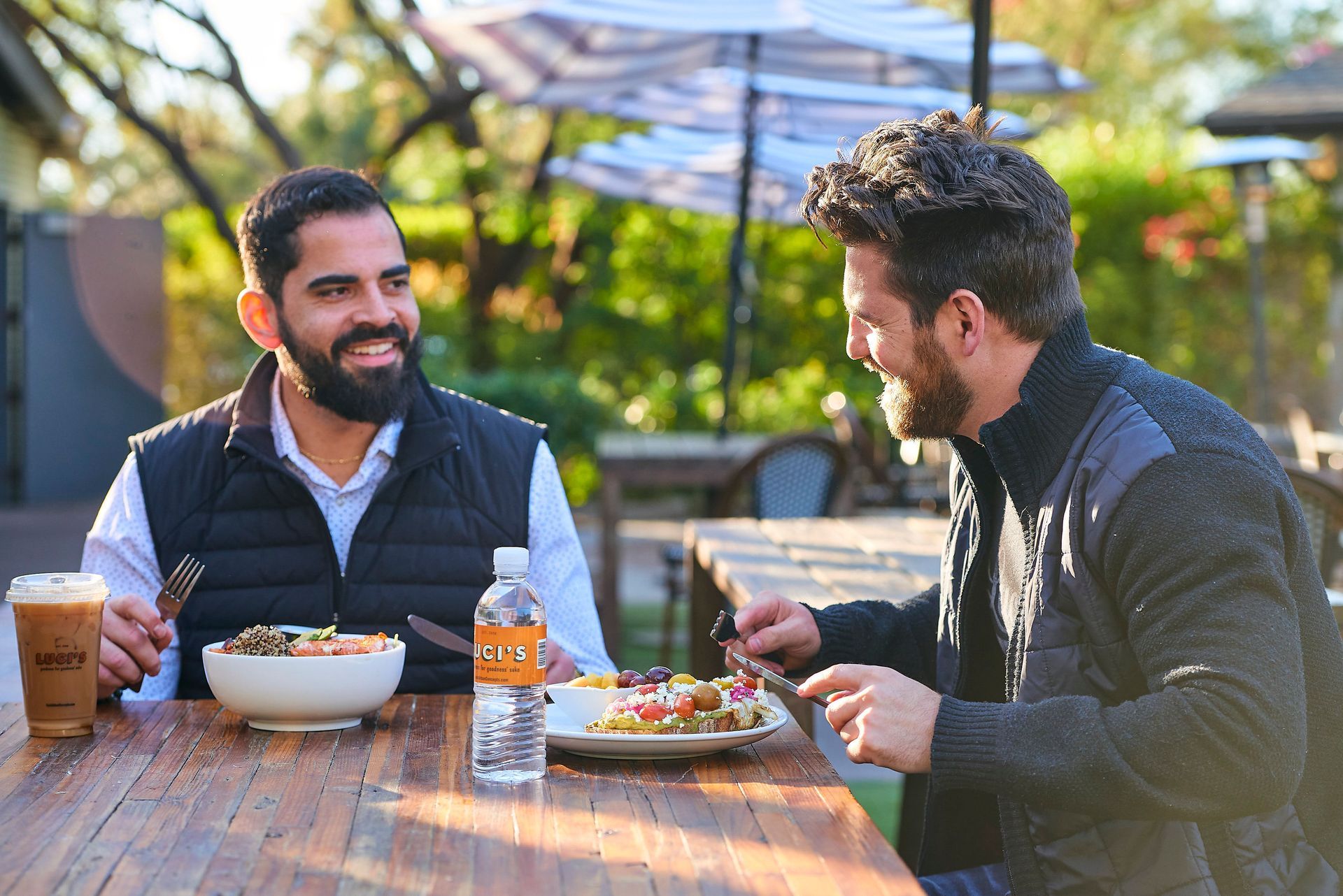 Two men are sitting at a table eating food and drinking water at Luci's at the orchard