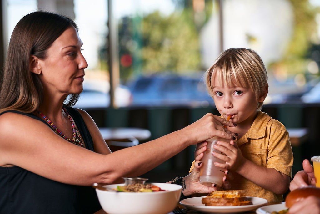 A woman is feeding a child a drink while sitting at a table in a restaurant.
