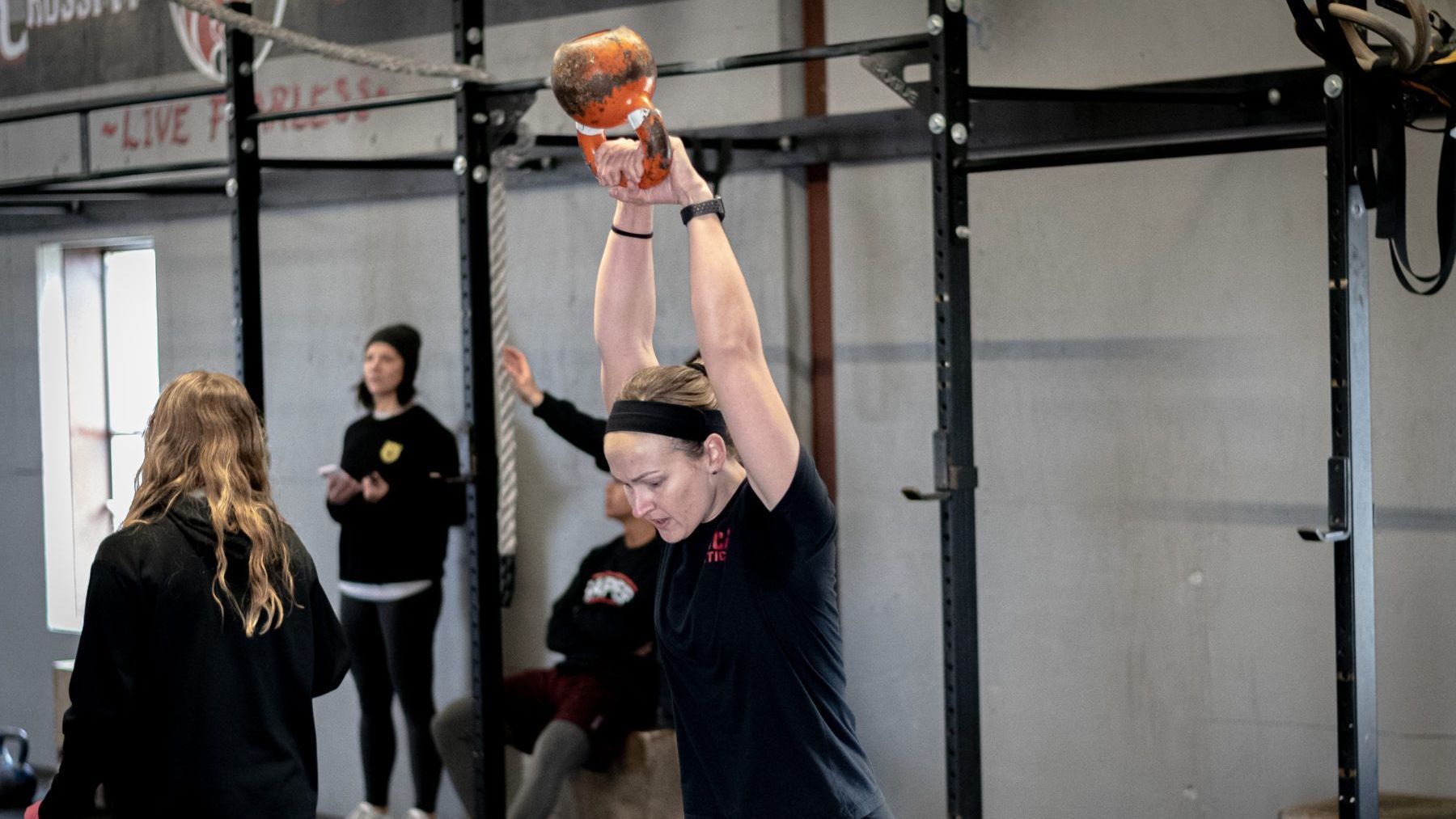 A woman is lifting a ball over her head in a gym.