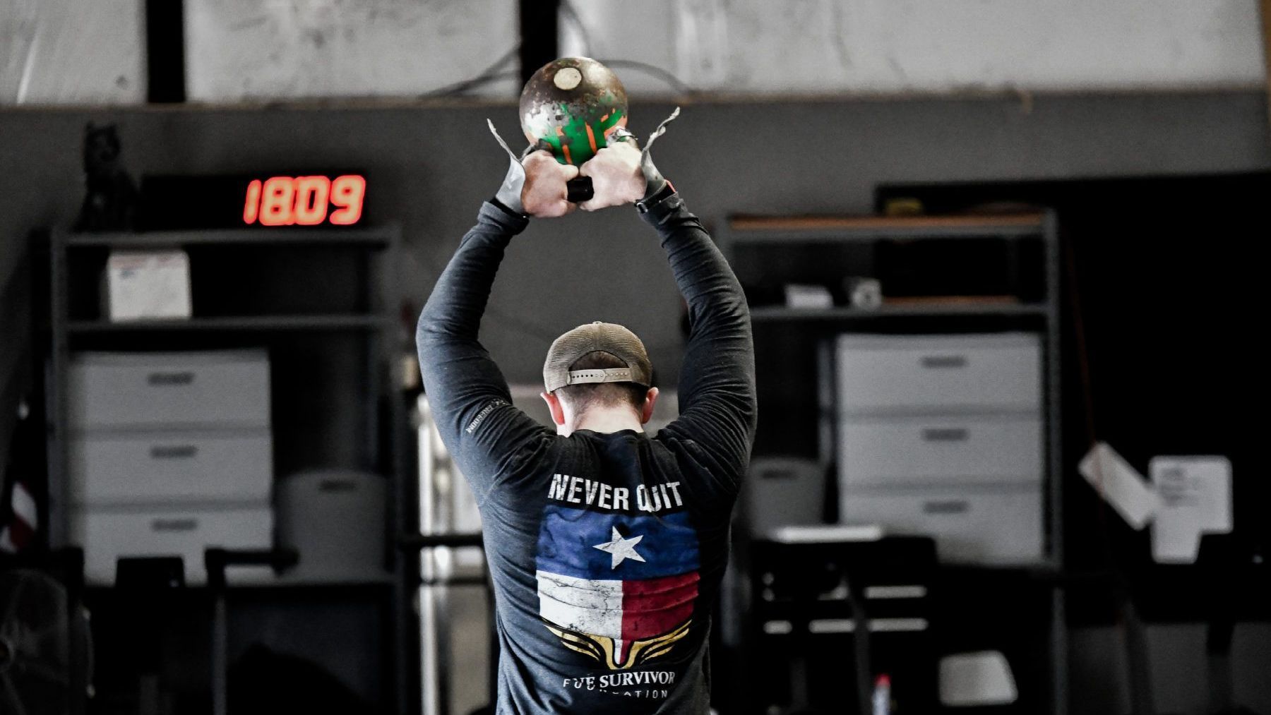 A man is holding a kettlebell over his head in a gym.