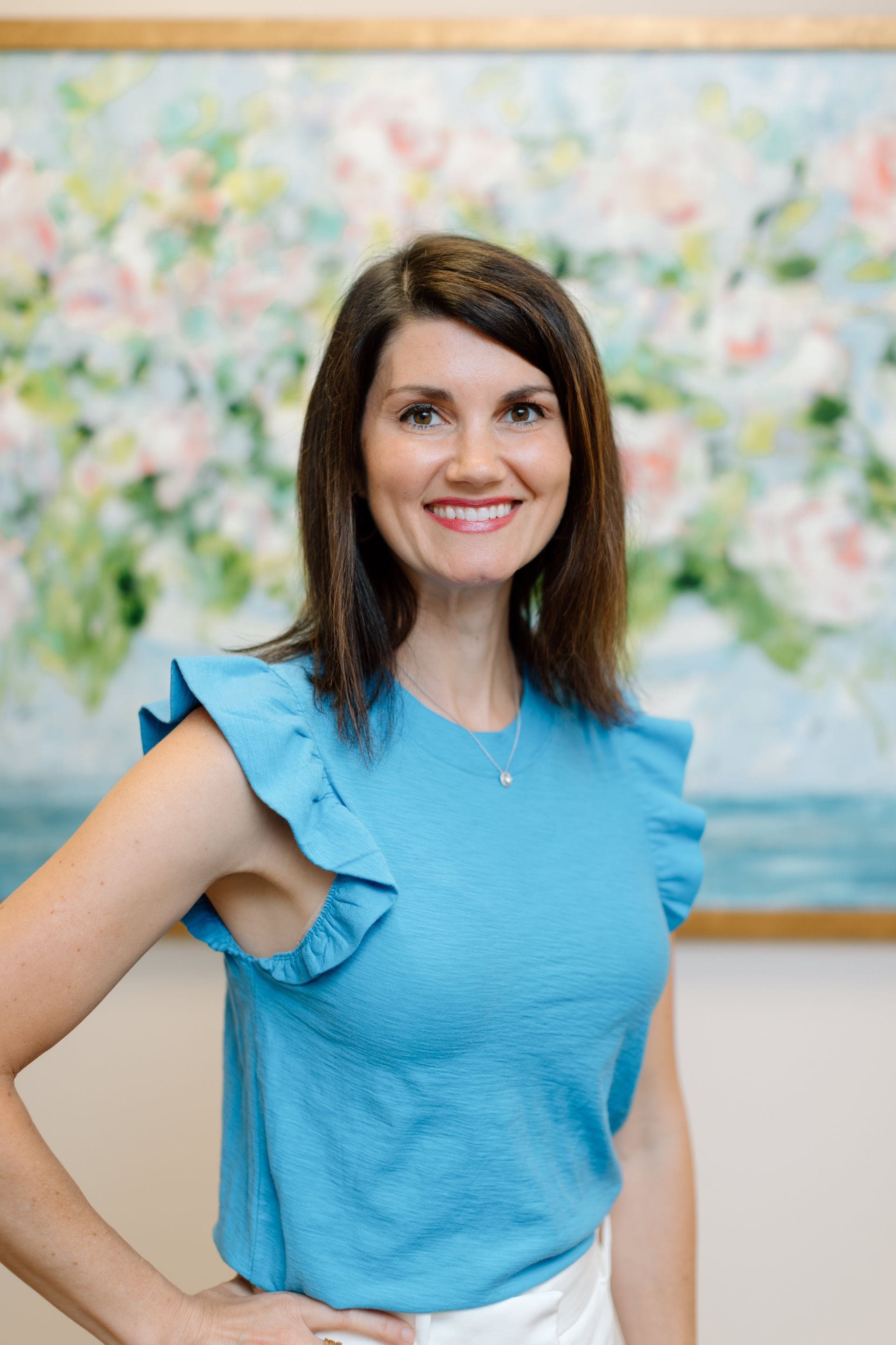 A woman in a blue shirt is standing in front of a painting.