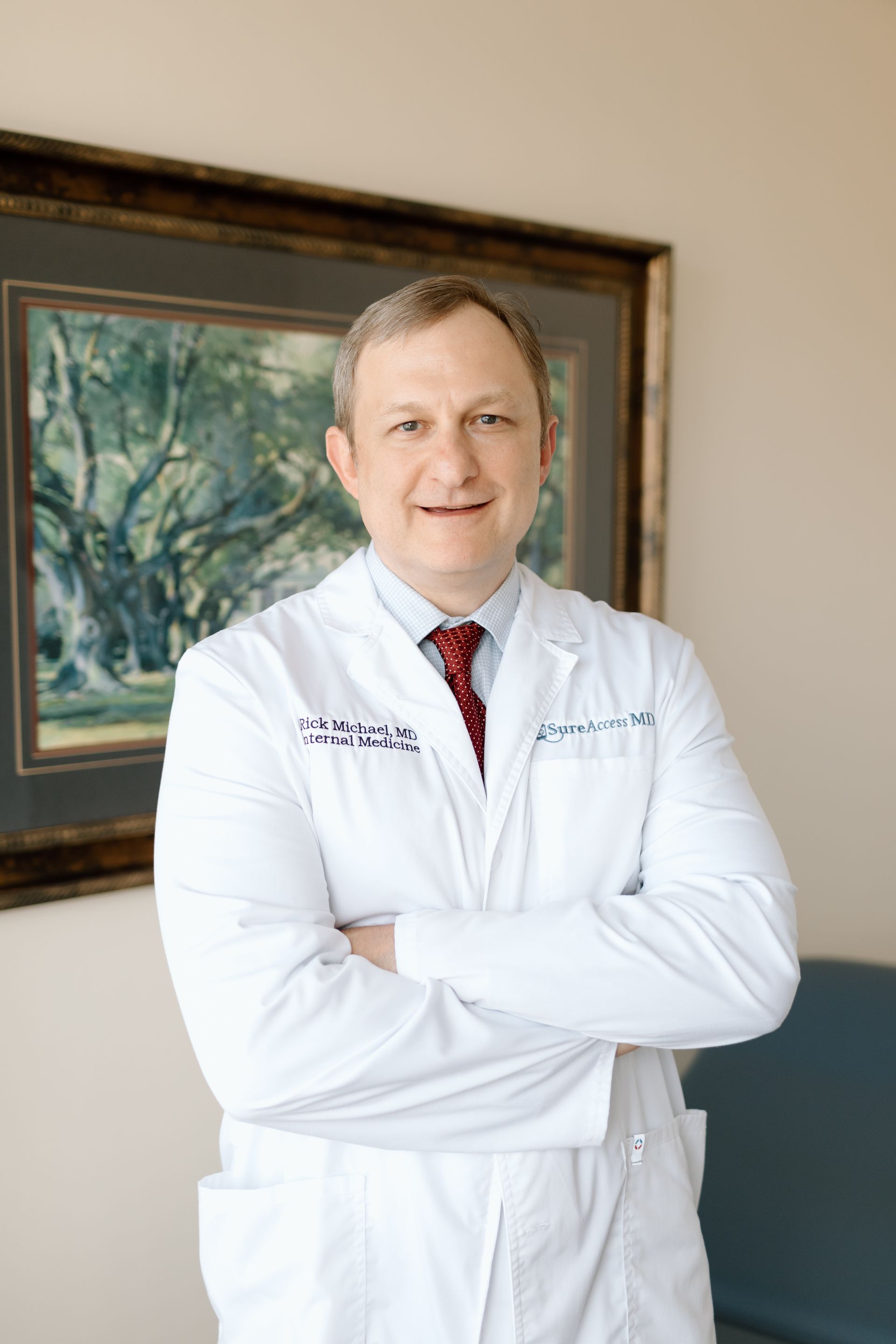 A man in a white coat and tie is standing with his arms crossed.