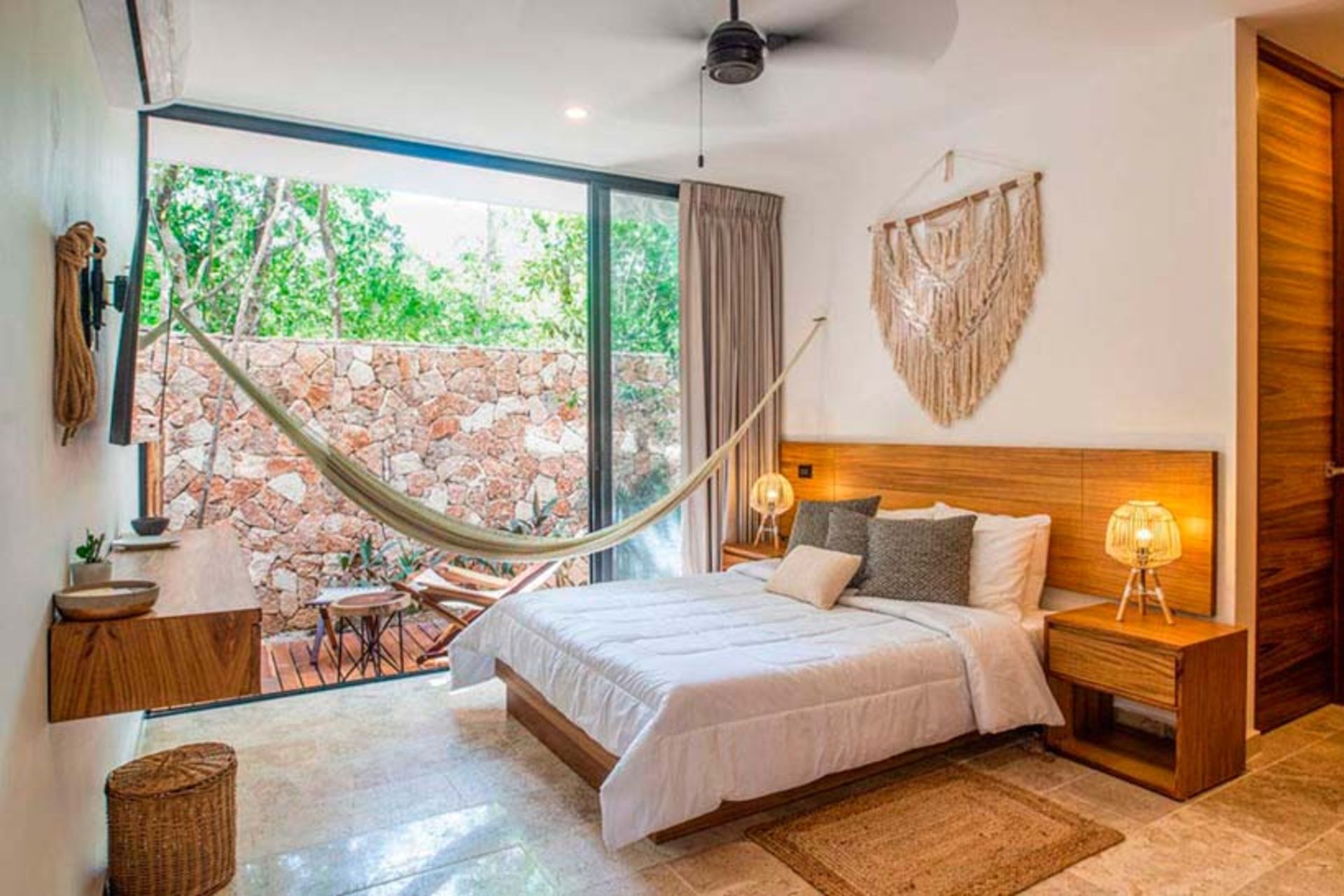 Dormitorio con cama, hamaca, ventana grande, detalles en madera y macramé decorativo colgante.