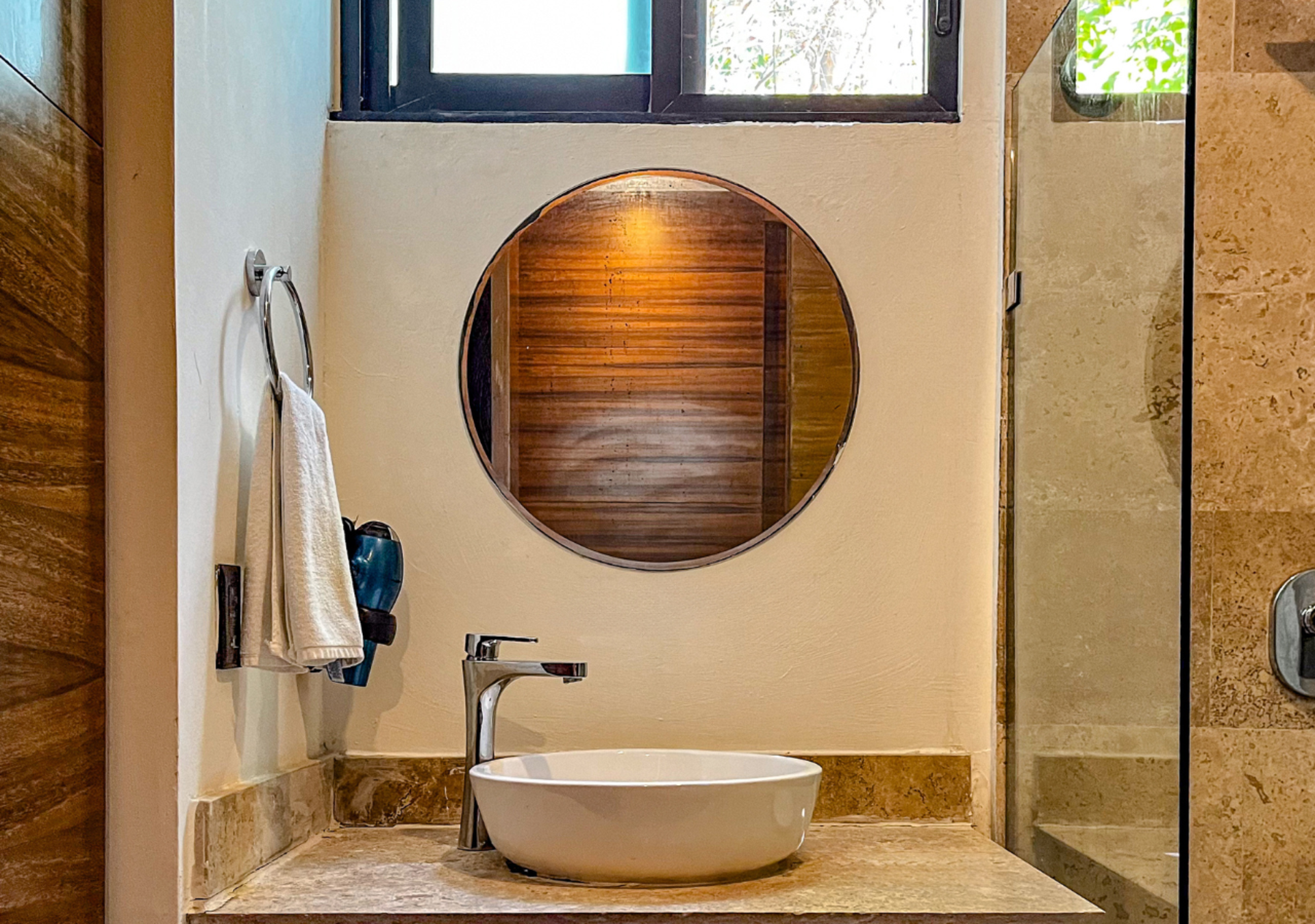 Lavabo de baño con espejo redondo y toallero; encimera y pared en color tostado.