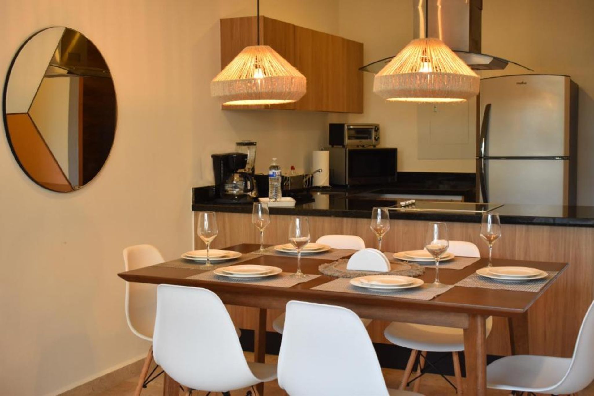 Comedor con mesa puesta para seis, cocina con electrodomésticos y espejo circular.