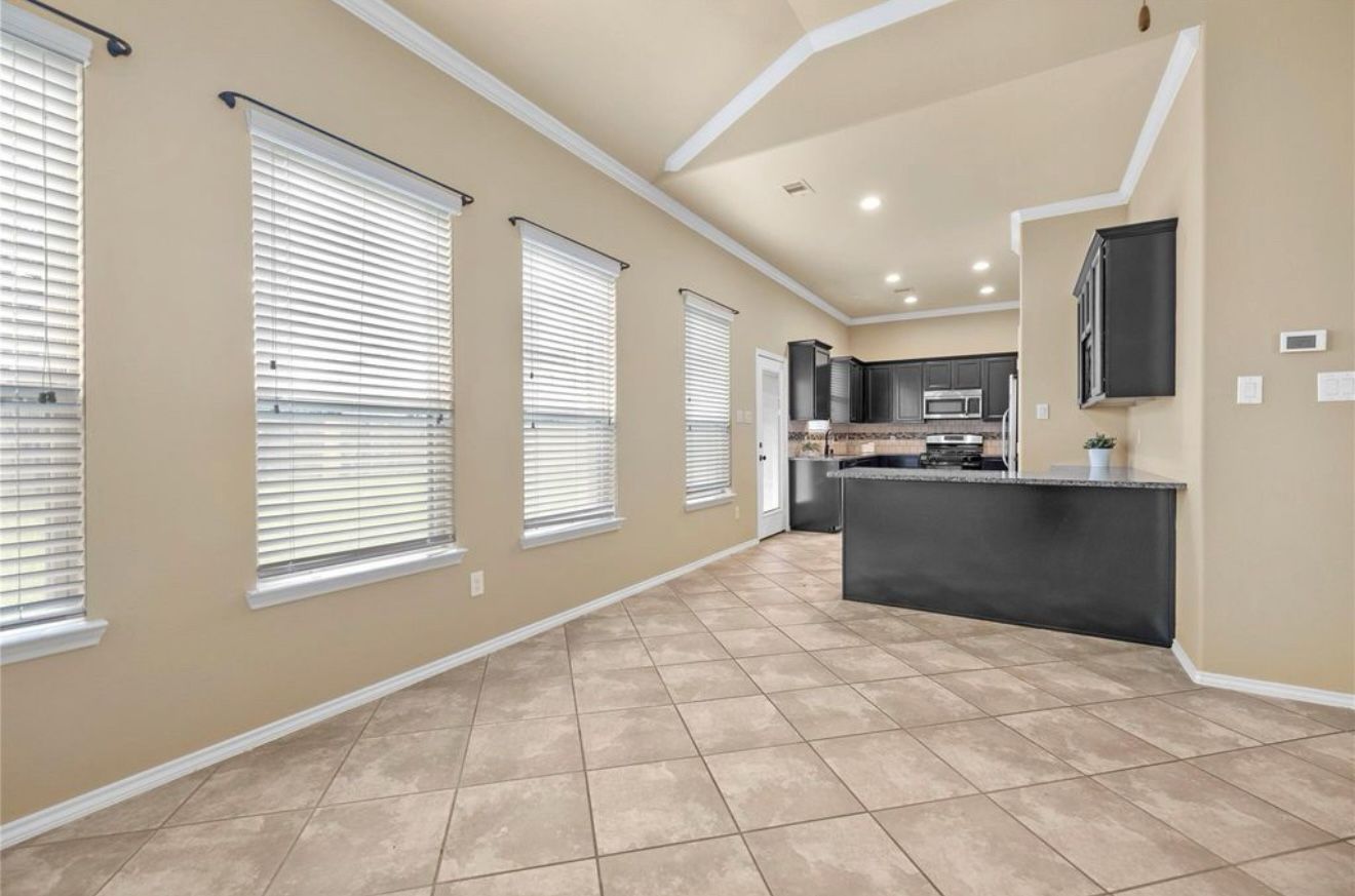 An empty living room with tile floors and a kitchen in the background.