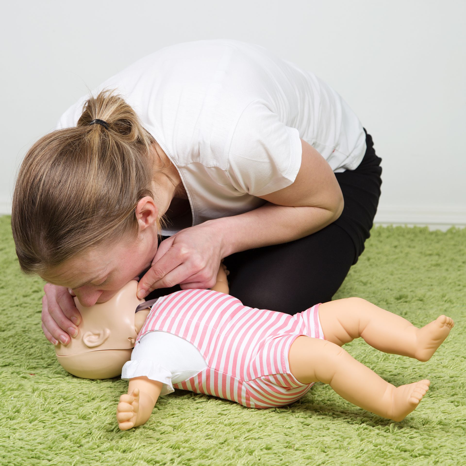 Three people practice CPR on a training mannequin in a classroom.