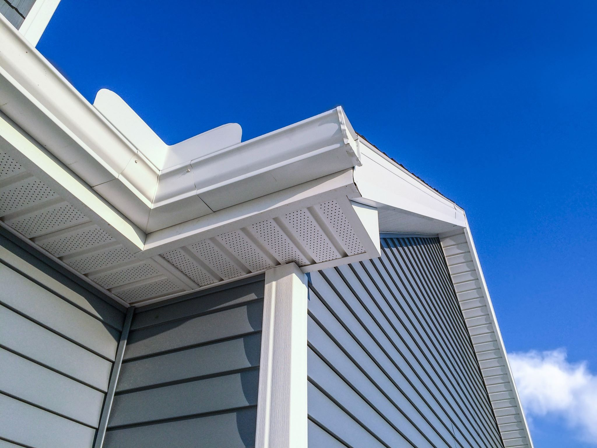 Corner of a house with gray siding, white trim, and a bright blue sky.