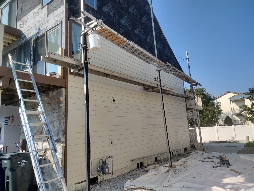 Construction of siding on a house. Scaffolding, ladder, new siding installed. Overcast sky.
