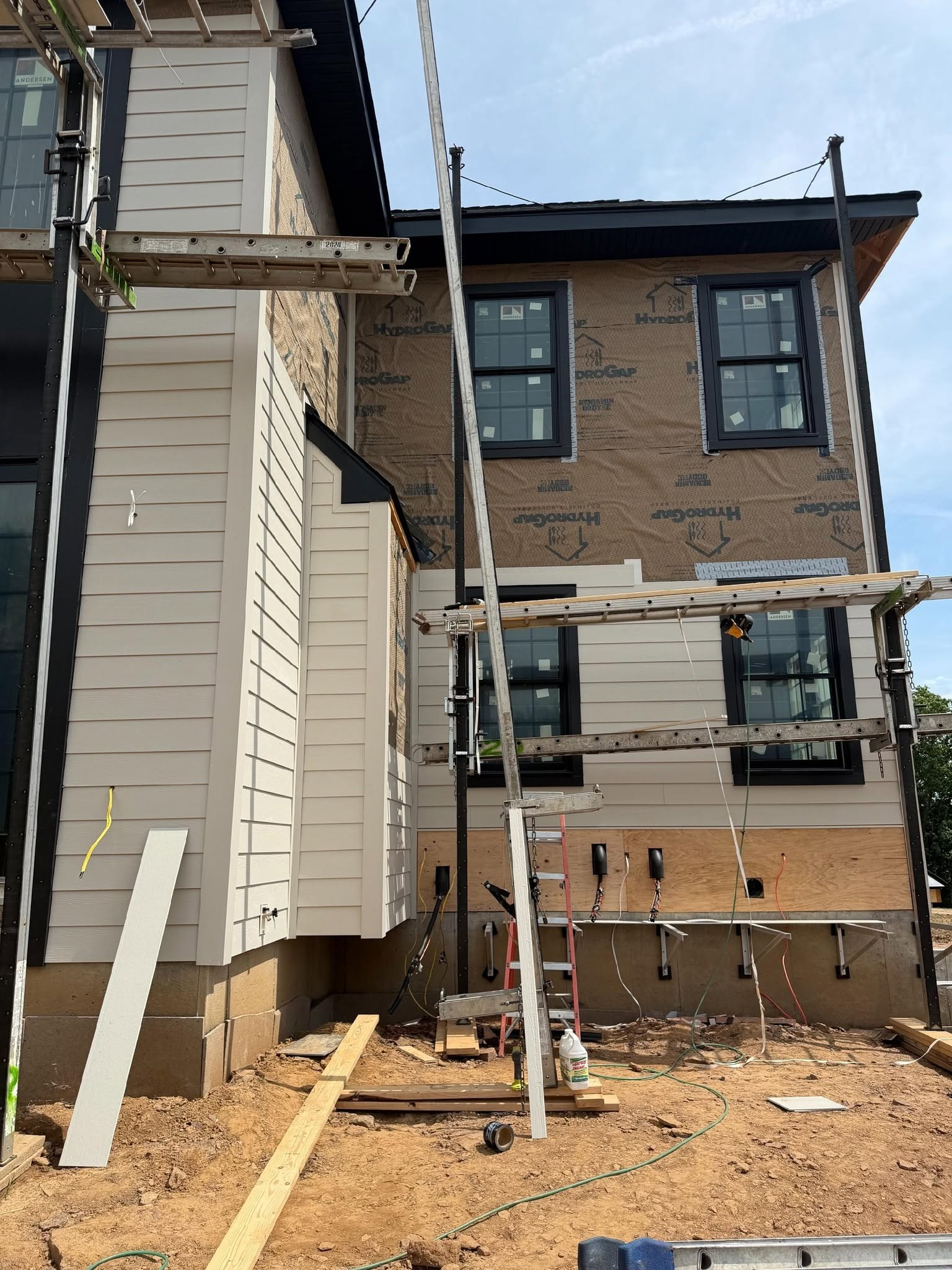 Construction tools and helmet on ladder prepared for siding repair project on modern home wall.