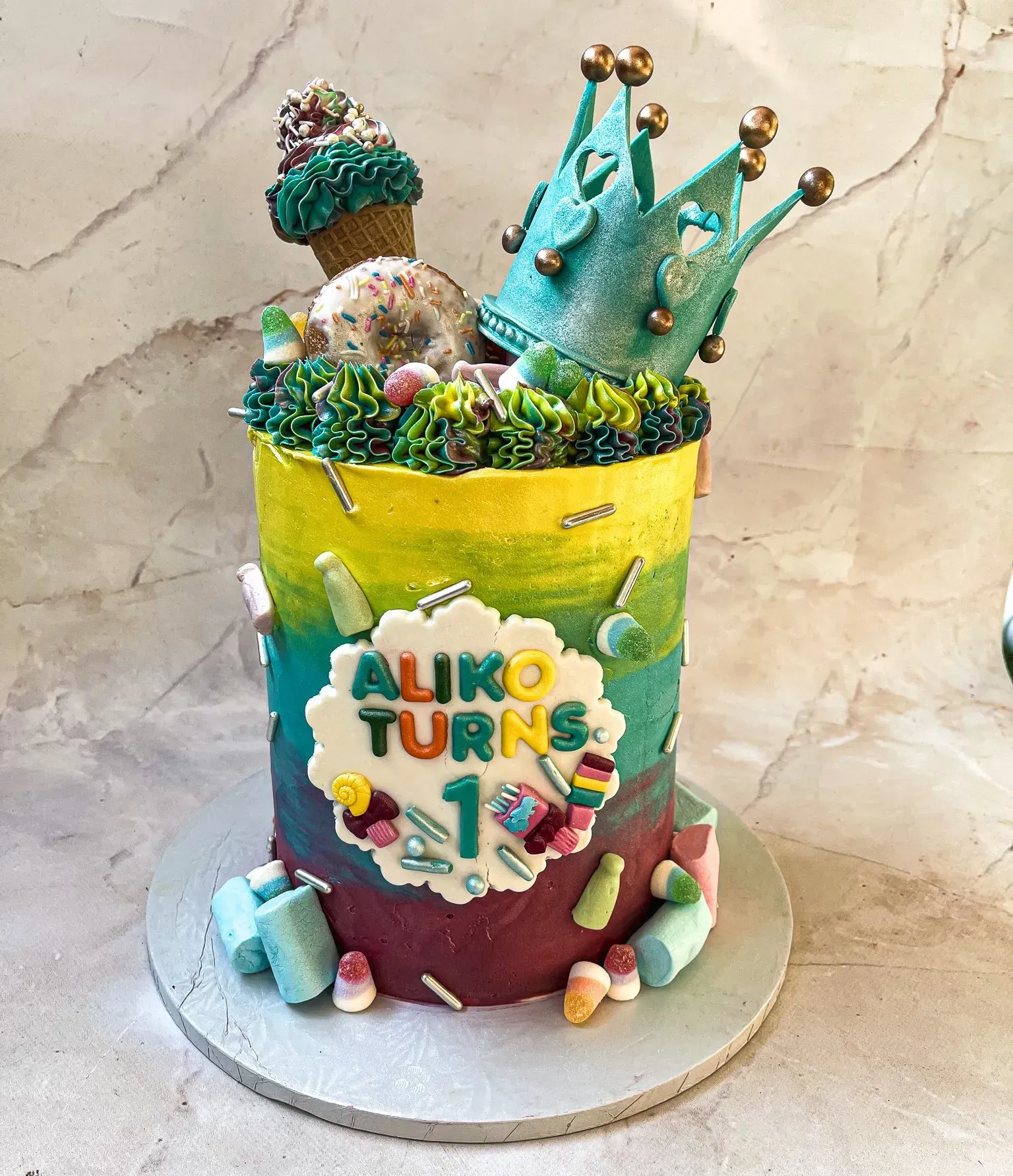 Birthday cake with colorful frosting, sweets, and turquoise crowns on top. Text says 